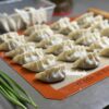 a tray of dumplings on a mat with green onions